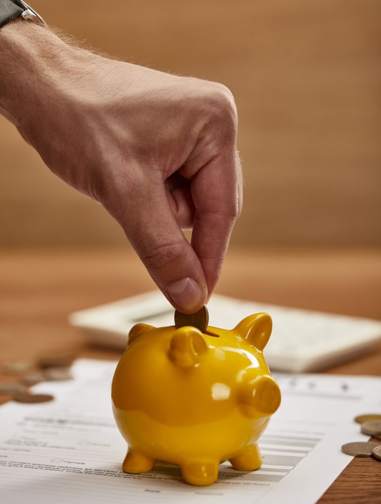 partial view of man putting coin in yellow piggy bank