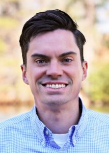 Portrait of a smiling man in a blue checkered shirt.