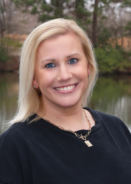 Blonde woman smiling outdoors with a gold necklace.