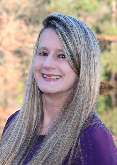 Professional headshot of smiling woman with long blonde and gray hair.