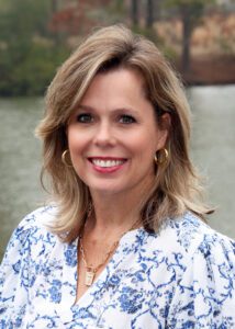 Portrait of a smiling woman with blonde hair wearing a blue and white patterned blouse.